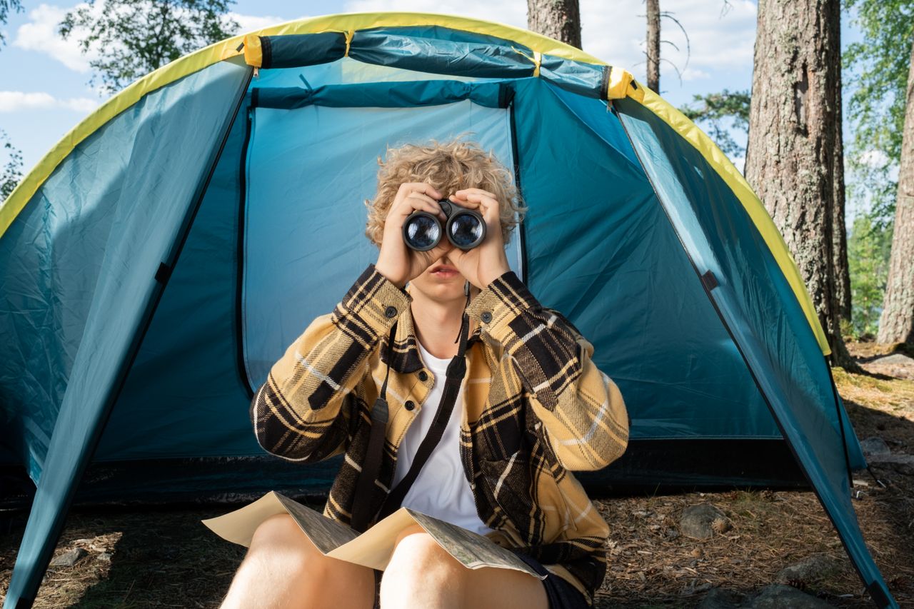Teen camping with binoculars and a map, exploring the outdoors in summer.