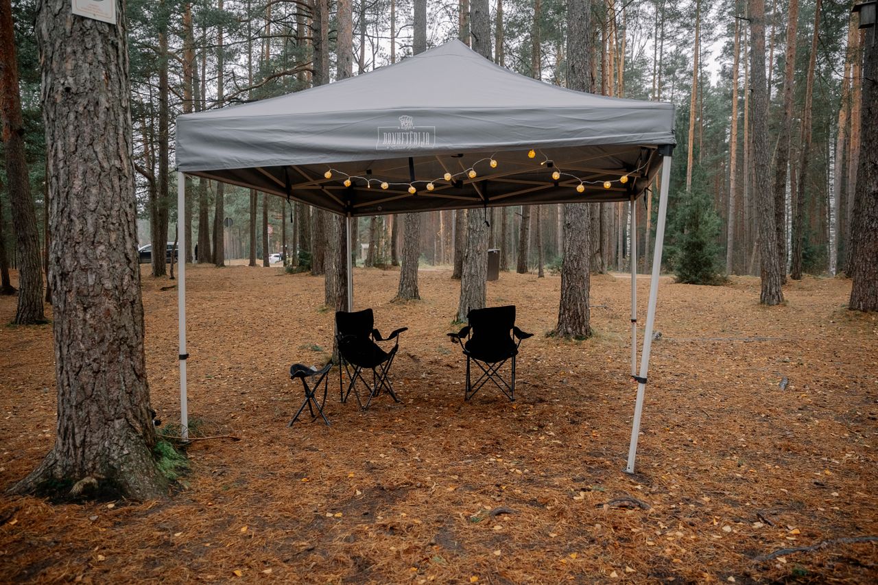 A serene forest campsite with a canopy tent and chairs, perfect for outdoor relaxation.