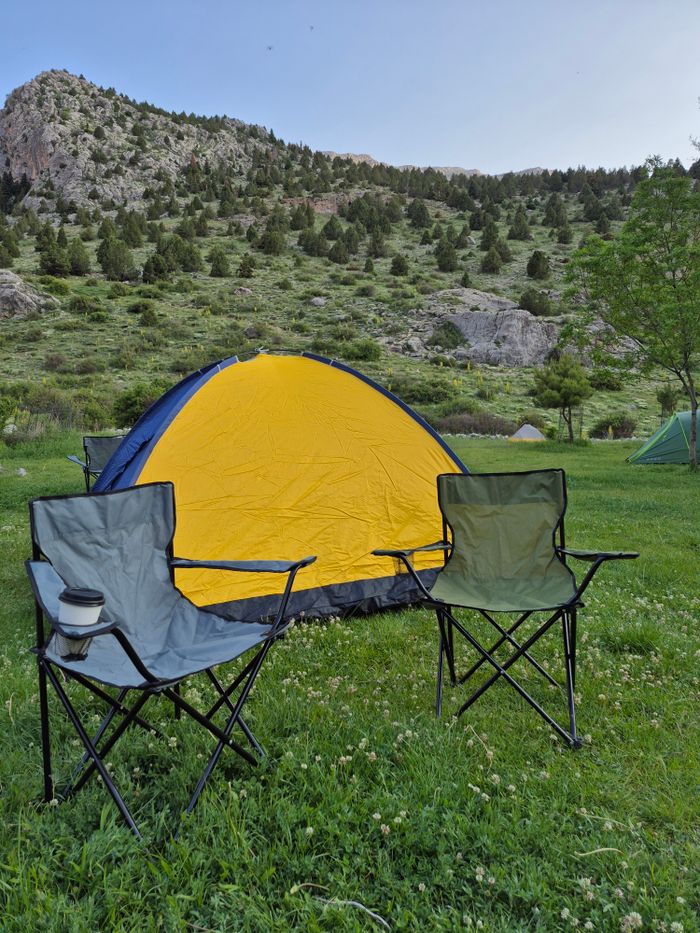 A serene campsite with a tent and chairs against a mountain backdrop, perfect for outdoor adventures.